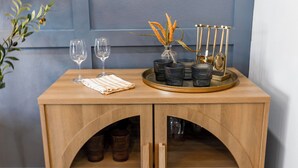 Un mobile in legno con portabottiglie, un vassoio con bicchieri e tazze, e un vaso con fiori.