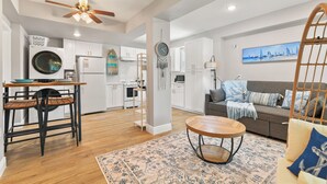 A modern kitchen with white cabinets, a built-in washer and dryer, and a dining area with a wooden table and chairs.