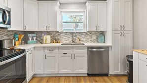 A modern kitchen with white cabinets, a stainless steel dishwasher, and a window above the sink.