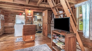 A cozy cabin interior with a kitchen, a dining area, a living room with a TV, and a bookshelf.