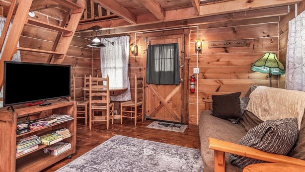 A cozy cabin interior with a wooden TV stand, bookshelves, a sofa, and a dining area with chairs.