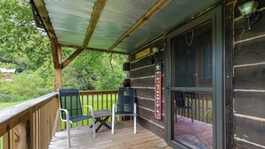 A wooden deck with two chairs and a table, a welcome sign, and a view of the surrounding greenery.
