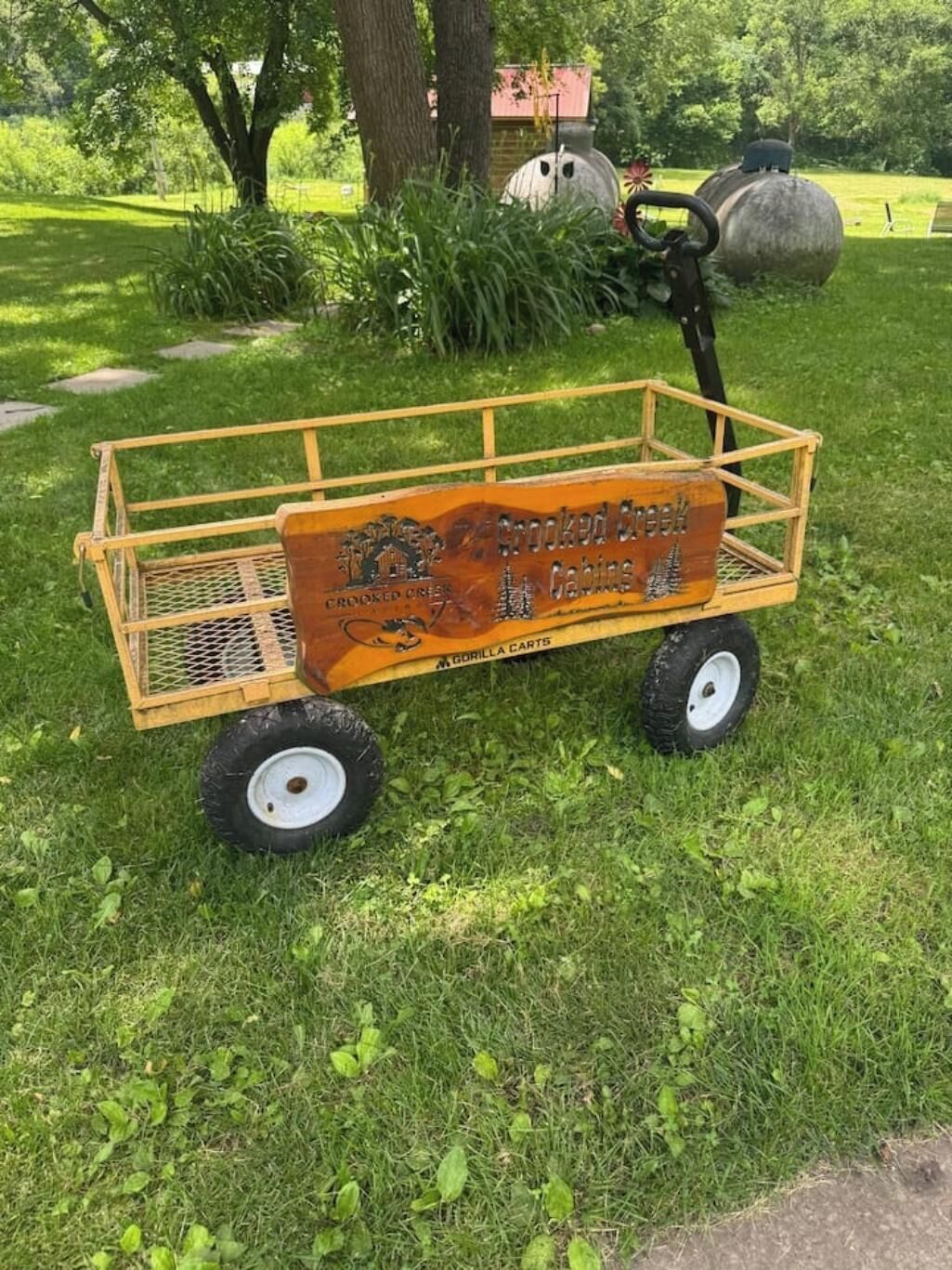 A wooden cart with a sign that reads "Crooked Creek Cabins" and "Gorilla Carts" on a grassy area.