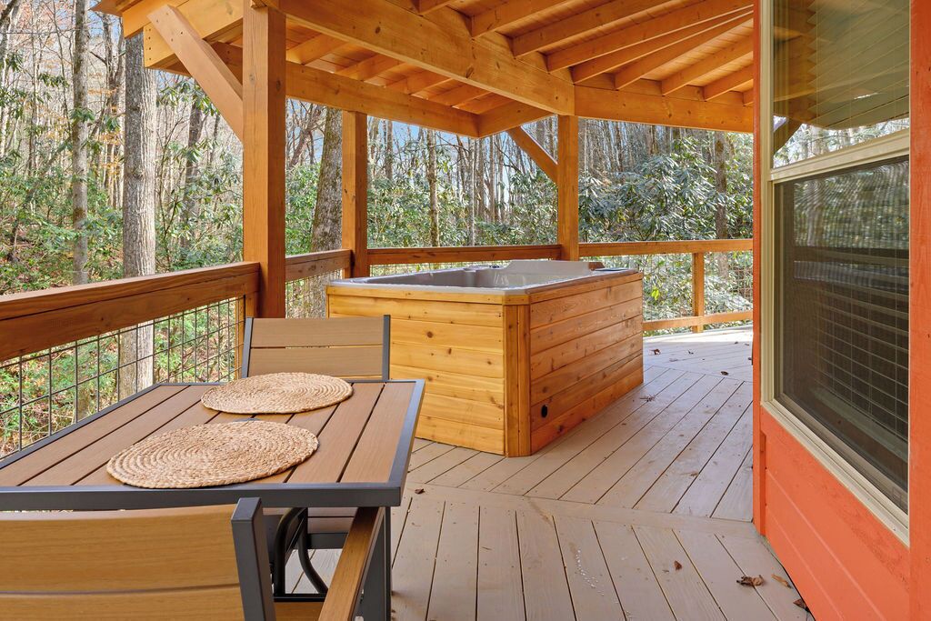 Eine Holzterrasse mit Whirlpool, einem Tisch mit gewobenen Unterlagen und Blick ins Waldgebiet.