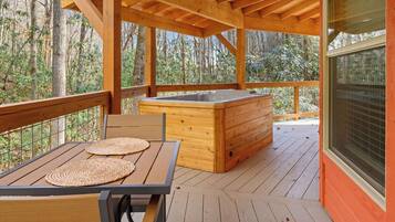 Eine Holzterrasse mit Whirlpool, einem Tisch mit gewobenen Unterlagen und Blick ins Waldgebiet.
