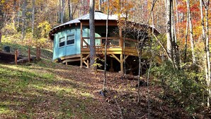 A cabin with a wooden deck and a small porch, surrounded by trees with autumn foliage.