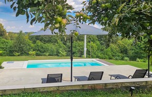 Piscina con sillas de descanso y una zona cubierta, rodeada de vegetación.