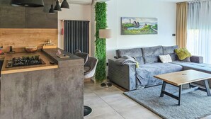 A modern living room with a grey sofa, a coffee table, and a kitchen area with a countertop and stove.