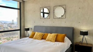 Ein modernes Schlafzimmer mit einem großen Bett, zwei Nachttischen und Blick auf die Stadt.