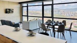 Eine moderne Küche mit einer langen Arbeitsplatte, Essbereich mit Stühlen und großen Fenstern mit Blick auf die Stadt.