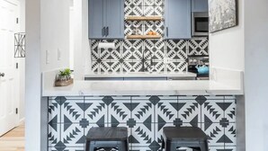A modern kitchen with geometric patterned tiles, grey cabinets, and a blue microwave.