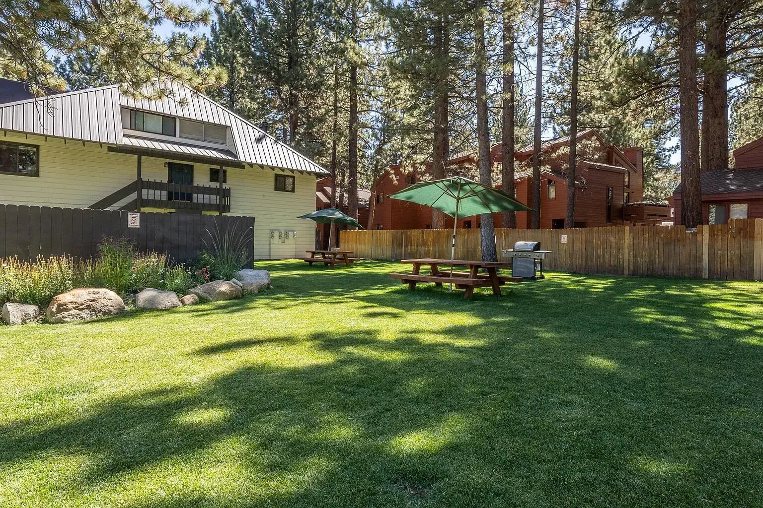 A backyard with a picnic table, a grill, and a wooden fence.