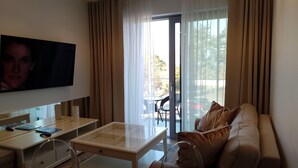 A modern living room with a flat-screen TV, a glass coffee table, a leather sofa, and a sliding glass door leading to an outdoor area with a table and chairs. - Apartment in Miedzyzdroje With Sea View (Międzyzdroje)