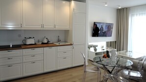 A modern kitchen with white cabinets, a wooden countertop, and a glass dining table with clear chairs. - Apartment in Miedzyzdroje With Sea View (Międzyzdroje)