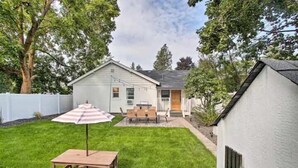 A backyard with a wooden table and chairs, a striped umbrella, and a white house with a porch. - Cheerful 3 bedroom Villa with Backyard Oasis (Spokane)