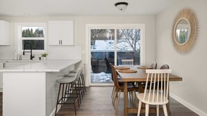 A modern kitchen with white cabinetry, a large island, and a dining area with wooden chairs and a table.