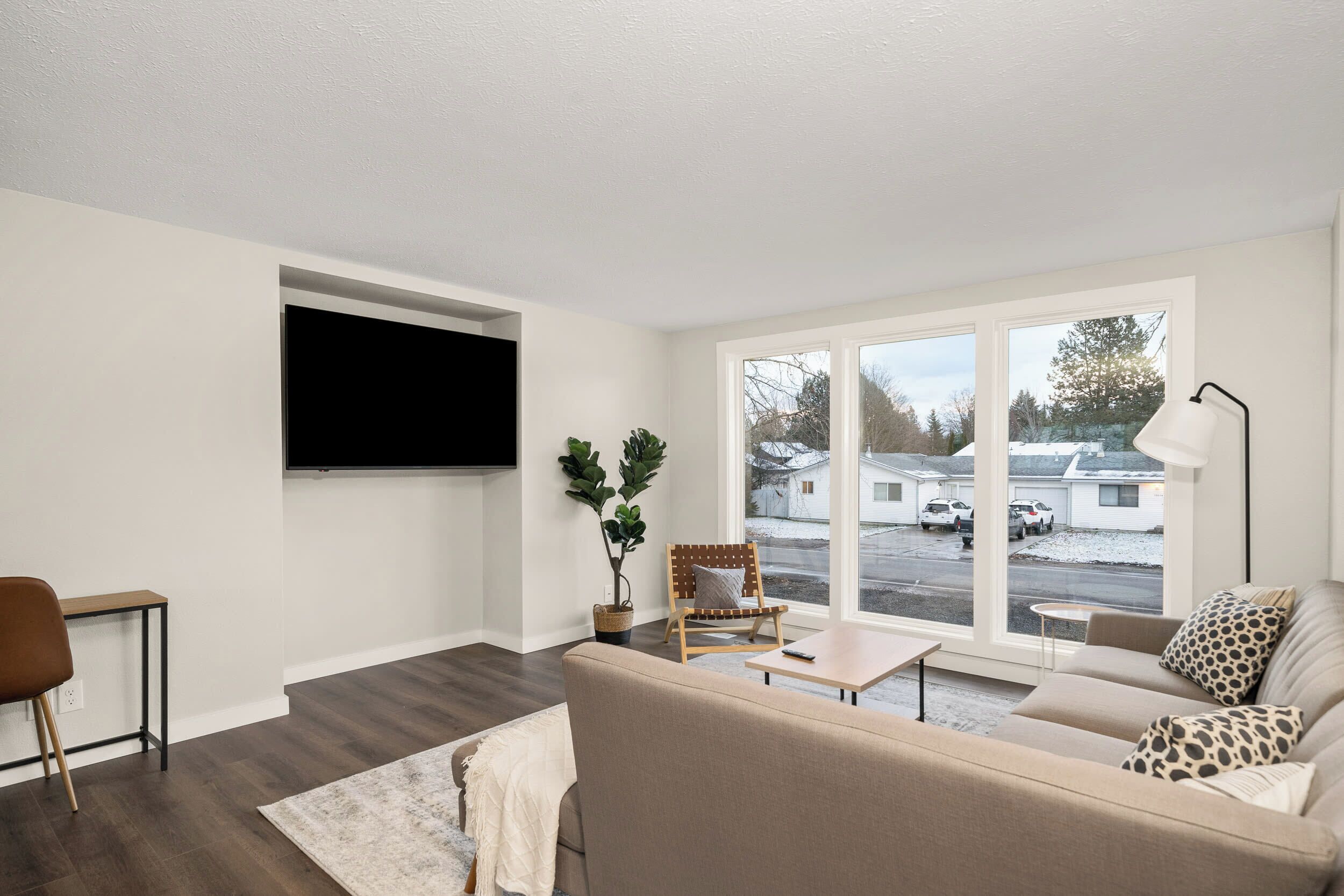 Una sala de estar moderna con un ventanal grande, un televisor de pantalla plana en la pared, un sofá, una mesa de centro y una silla.