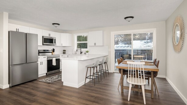 A modern kitchen with white cabinetry, stainless steel appliances, and a central island with bar stools.