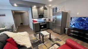 A modern living room with a sofa, a red couch, a coffee table, and a TV. - Charming Legal Suite Ensuite BSMT, Two Beds, Two Baths (Calgary)