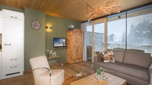 Una sala de estar acogedora con un sofá, una silla, una mesa de centro de madera, un televisor y un mueble de madera.