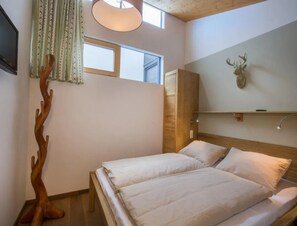 A bedroom with a bed, a wooden headboard, a mounted deer head, and a window with curtains. - Contemporary Alpine Stay in Neukirchen (Neukirchen am Grossvenediger)