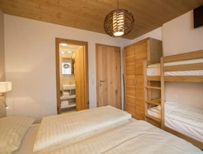 Une chambre avec deux lits, une armoire en bois et une salle de bain visible à travers une porte ouverte.