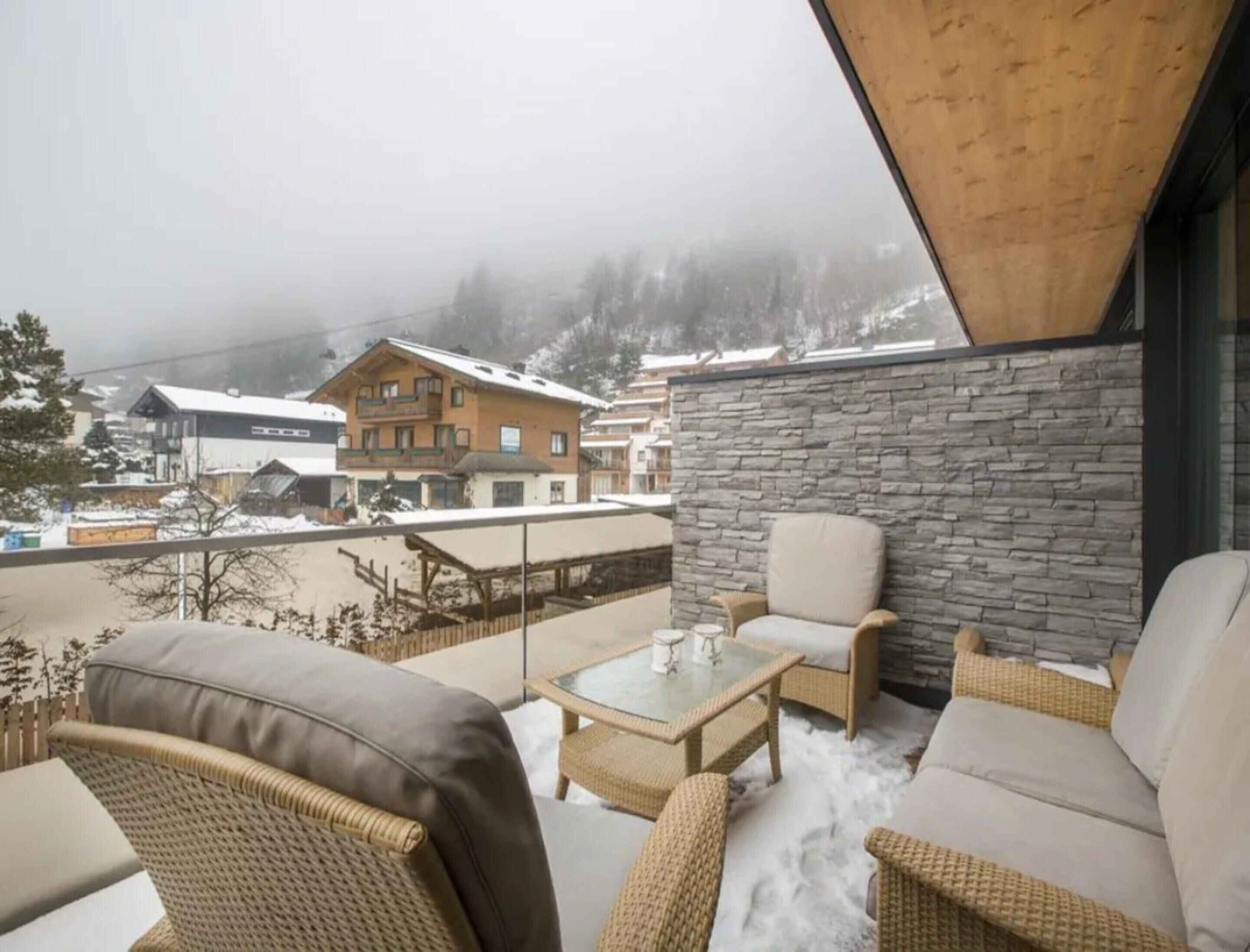 A snow-covered outdoor seating area with wicker furniture and a stone wall backdrop.
