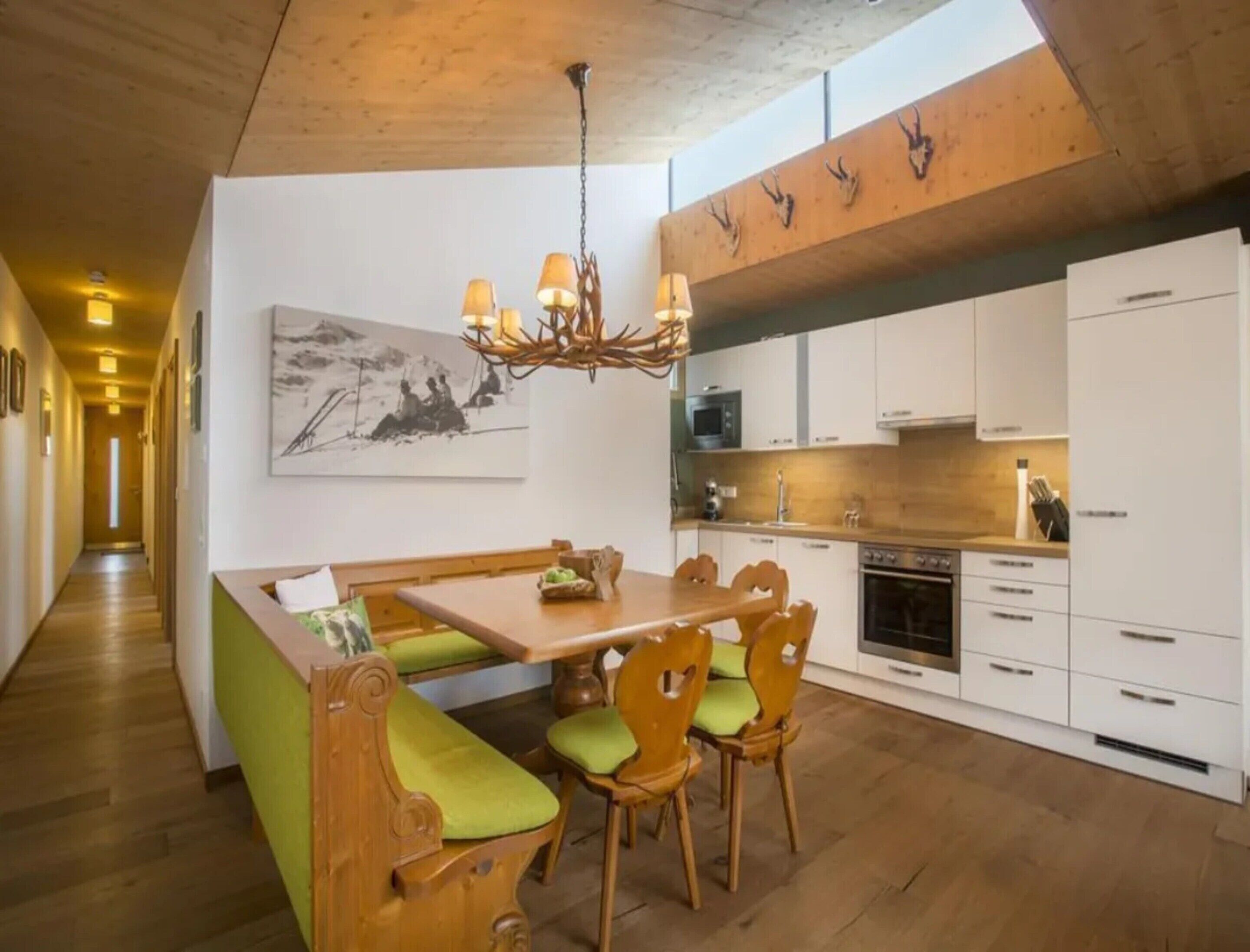 Una cocina moderna con una isla de madera, armarios blancos y un área de comedor con bancos acolchados verdes.