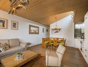 A cozy living room with a sofa, a wooden coffee table, and a dining area with a bench and chairs. - Contemporary Alpine Stay in Neukirchen (Neukirchen am Grossvenediger)