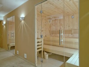 Un sauna avec un banc en bois, des portes en verre et un miroir au mur.