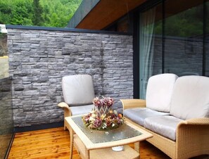Un balcón con pared de piedra, un sofá de mimbre, una mesa de centro de vidrio y un arreglo floral decorativo.