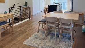 A spacious kitchen with a dining area, wooden flooring, and a staircase leading to an upper level. - Skip Rock Retreat | Near SLC | Cozy Mid-Term Stay (South Jordan)