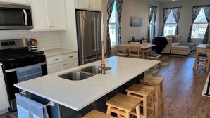 A modern kitchen with a central island, stainless steel appliances, and wooden stools. - Skip Rock Retreat | Near SLC | Cozy Mid-Term Stay (South Jordan)