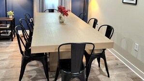 Uma sala de jantar com uma mesa comprida, cadeiras pretas e duas luminárias de chão.