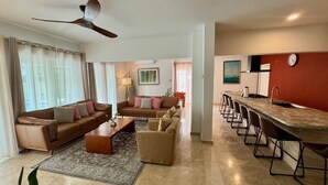 A modern living room with a sofa, armchairs, a coffee table, and a dining area with a long table and chairs.