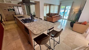 A modern kitchen with a central island, bar stools, and a dining area with a sofa.