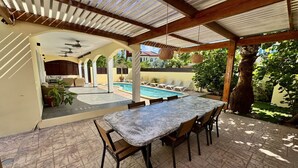 A covered outdoor dining area with a pool in the background.