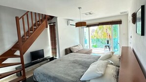 Une chambre avec un grand lit, un escalier en bois, une télévision et une fenêtre donnant sur un paysage verdoyant.