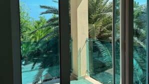 Un balcon doté d’une porte vitrée donnant accès à un espace piscine entouré de palmiers.