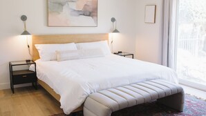 Un dormitorio con una cama grande, dos mesitas de noche, un banco, una ventana con vistas y un cuadro en la pared.