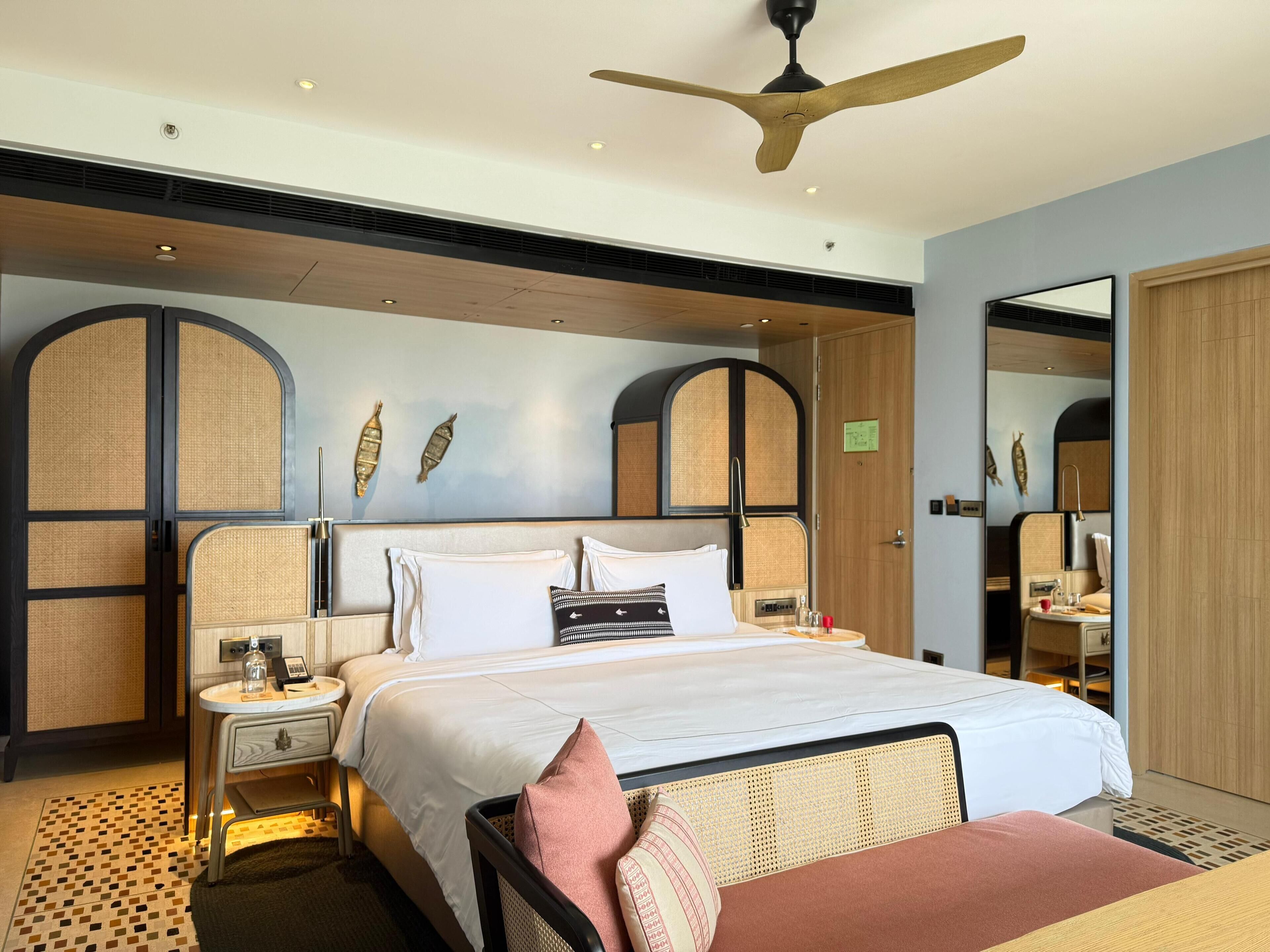 Une chambre d’hôtel comprenant un lit, des tables de chevet, un ventilateur de plafond et des panneaux décoratifs sur les murs.