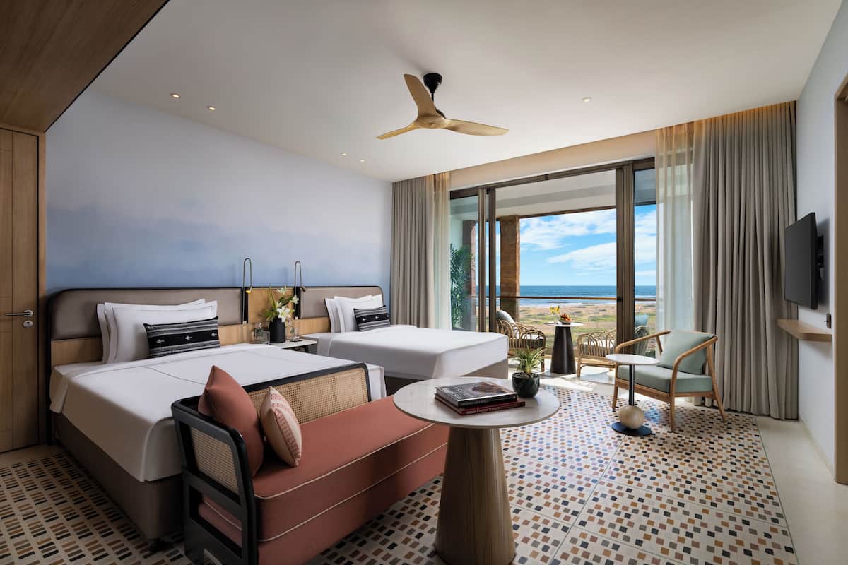 A hotel room with a bed, a sofa, a small table, a TV, and a view of the ocean.