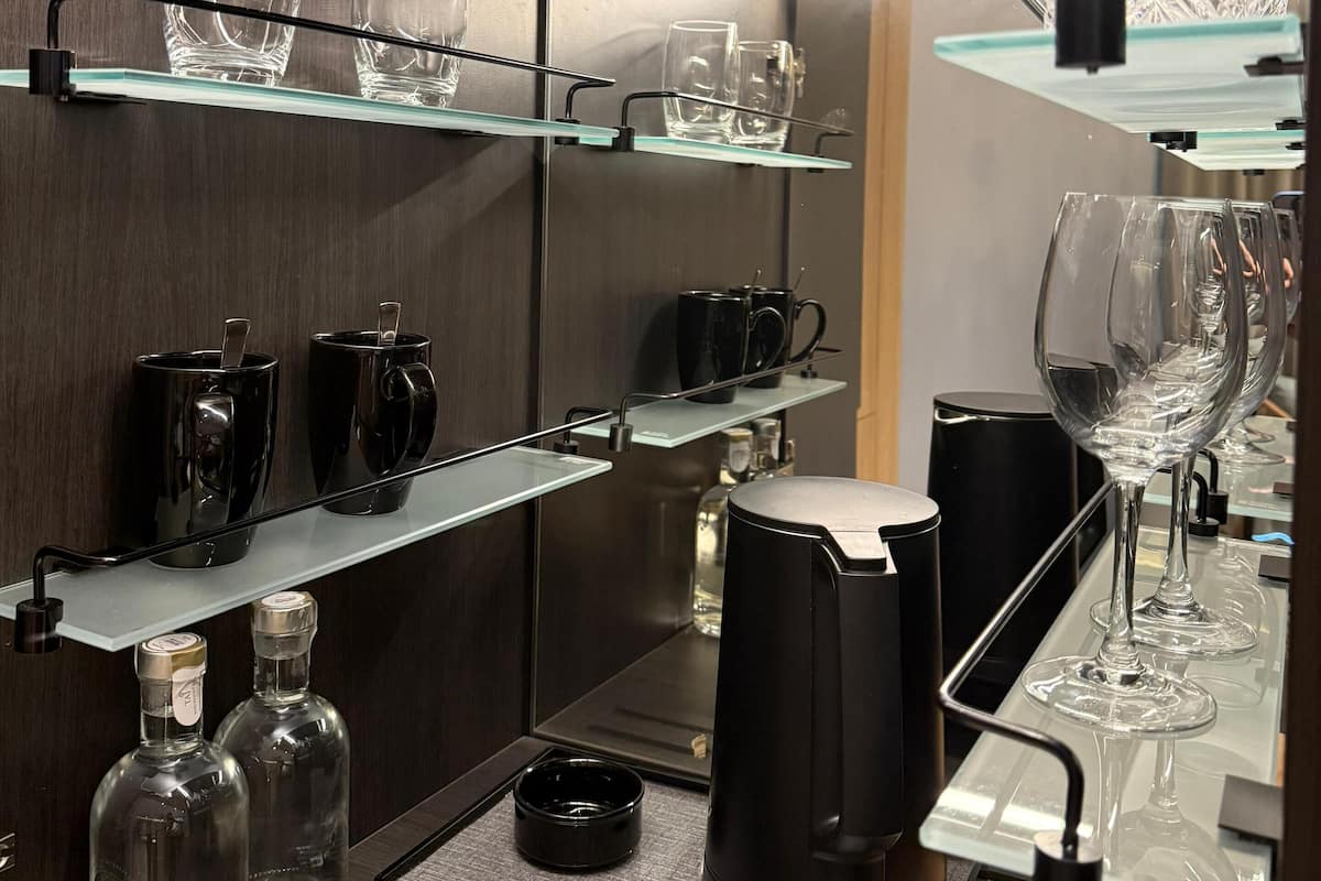 A modern kitchen with glass shelves holding various glassware, a coffee machine, and bottles.