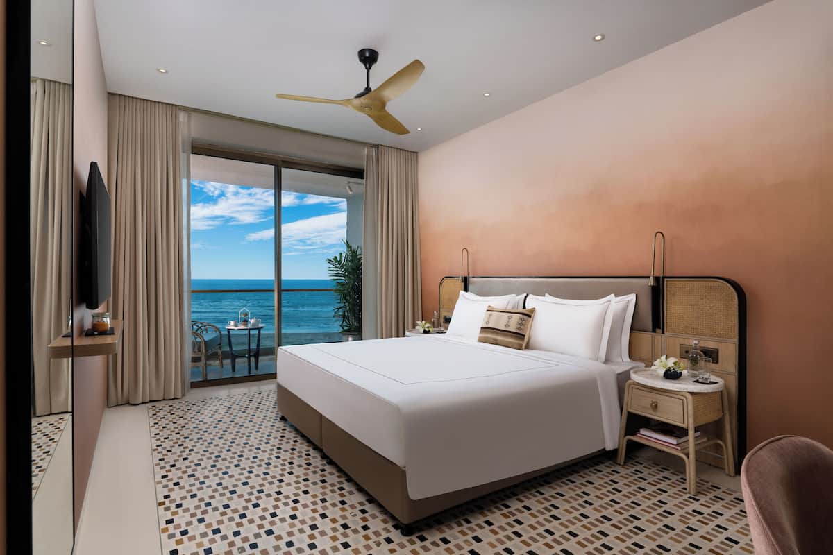 A hotel room with a large bed, a ceiling fan, a nightstand, and a view of the ocean.