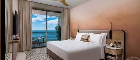 A hotel room with a large bed, a ceiling fan, a nightstand, and a view of the ocean.