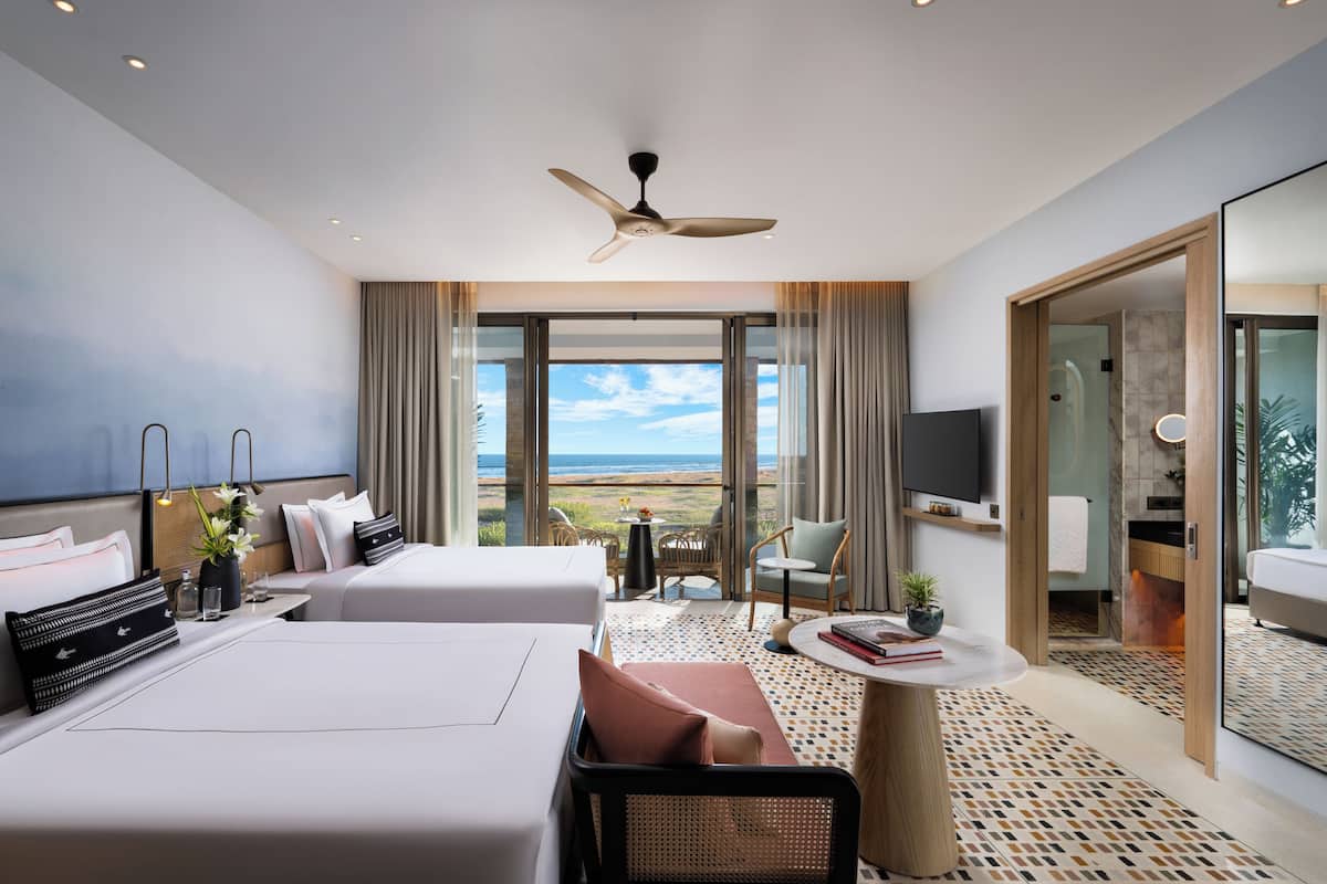 A modern hotel room with two beds, a balcony with a view, a ceiling fan, and a small table with a plant.