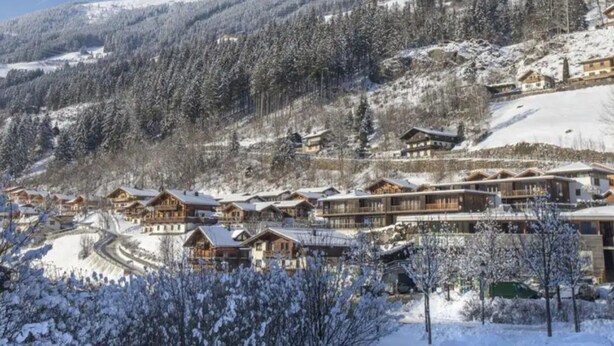 A snow-covered mountain resort with wooden chalets and a ski slope. - Zirbenholz Alpine Maisonette Stay (Wald im Pinzgau)