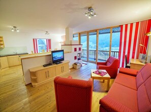 A modern living room with a television, red sofas, wooden flooring, and large windows offering a view of a snowy landscape. - Spacious Alpine Chalet in Wald im Pinzgau (Wald im Pinzgau)
