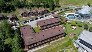 A multi-story building with a flat roof, surrounded by greenery and a parking area. - Zirbenholz Alpine Maisonette Stay (Wald im Pinzgau)