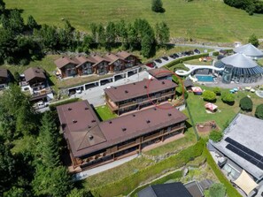 A multi-story building with a flat roof, surrounded by greenery and a parking area. - Zirbenholz Alpine Maisonette Stay (Wald im Pinzgau)